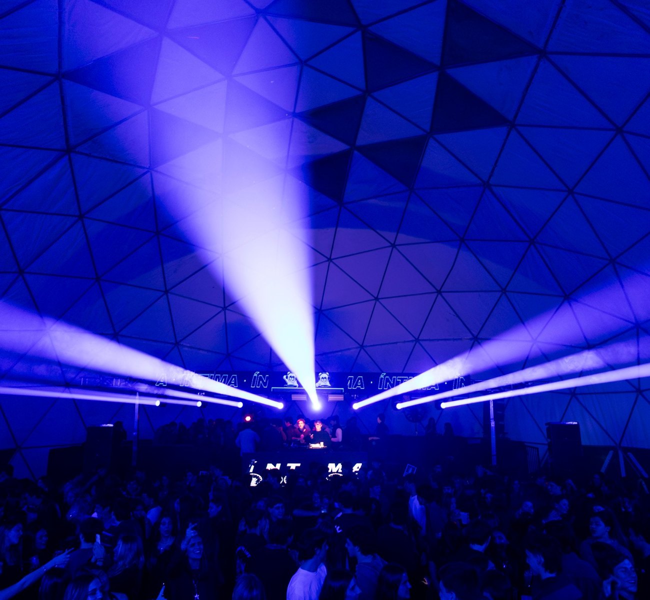 Fiesta de noche en Domo Point: la cúpula iluminada en azul con haces de luz sobre la pista llena